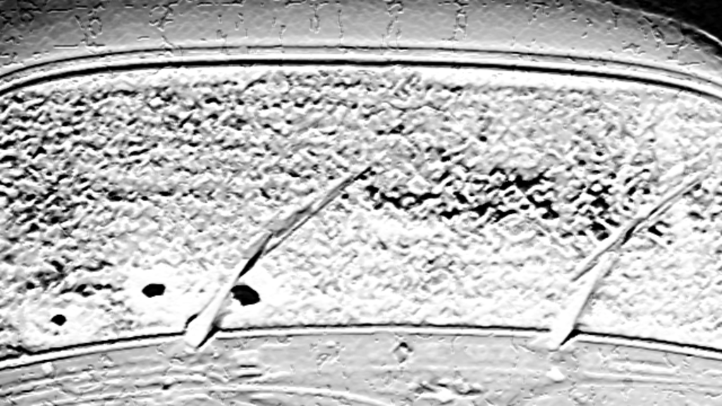 Imagem craquelada do vidro da frente de um carro fusca, em preto e branco. A imagem está em zoom.